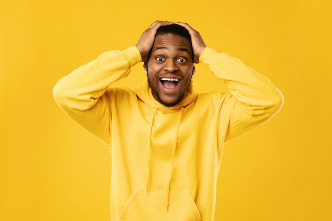 Excited Black Guy Shouting Touching Head Standing On Yellow Background