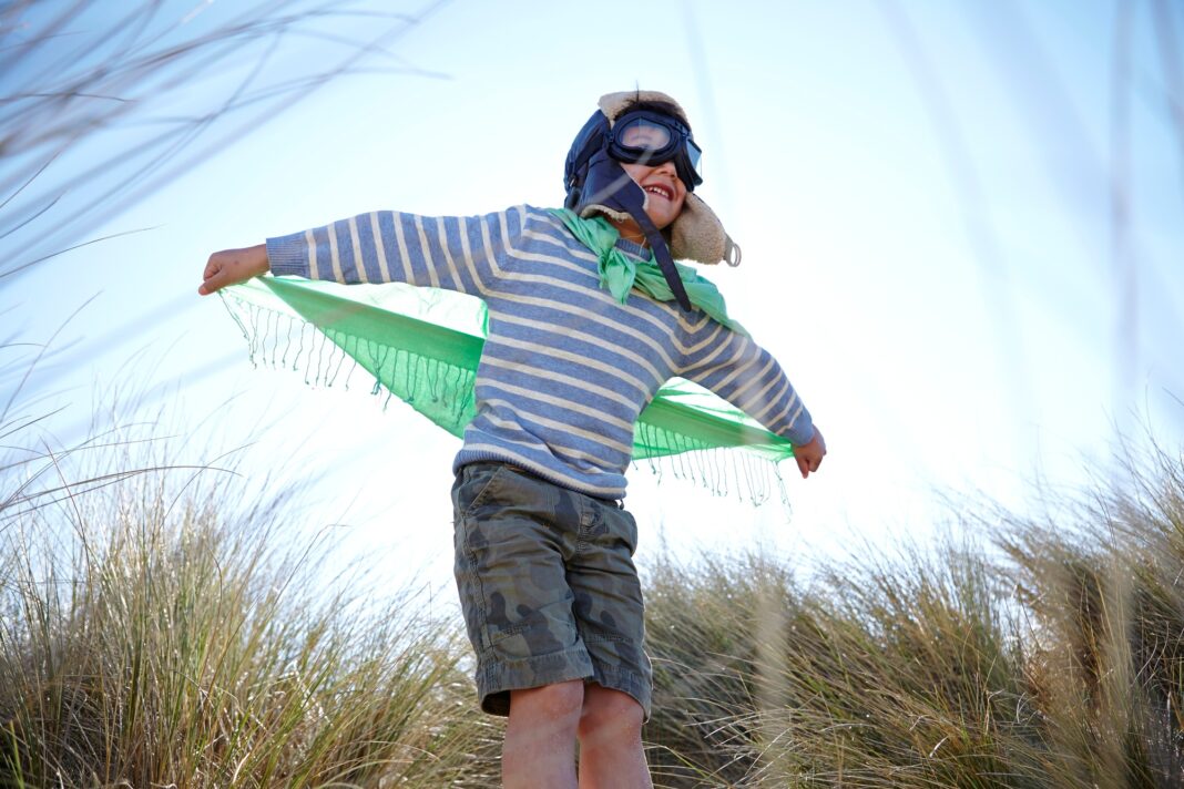 Young boy on beach, wearing fancy dress, pretending to fly